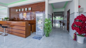 A reception area with a wooden reception desk, a refrigerator, potted plants, and a fire extinguisher.