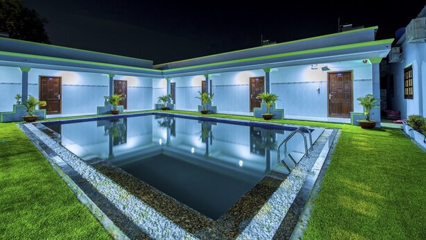 A poolside area with a rectangular pool, potted plants, and a building with multiple doors and windows.