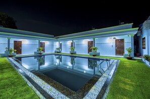 A poolside area with a rectangular pool, potted plants, and a building with multiple doors and windows.