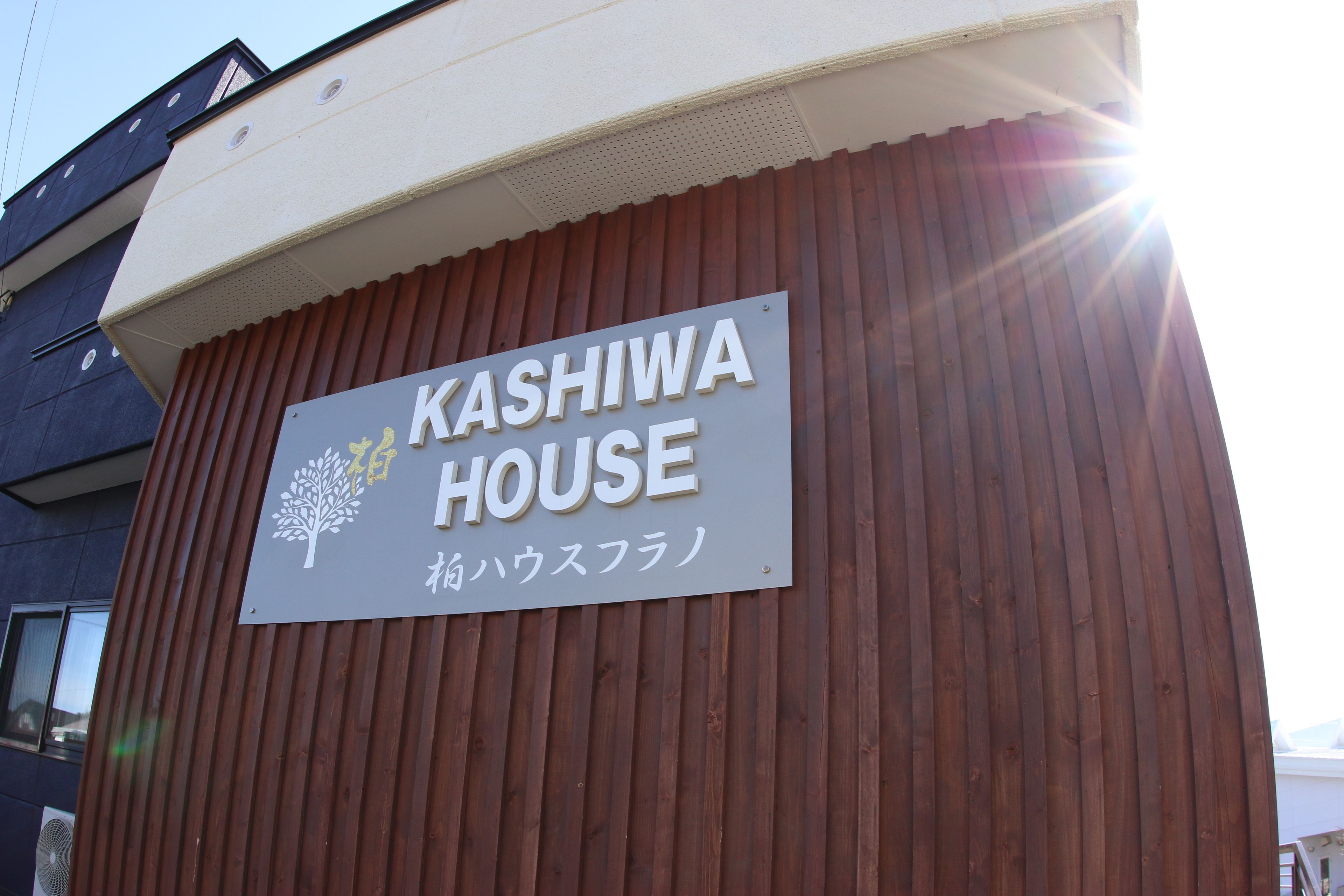 Letrero de KASHIWA HOUSE con un logotipo de árbol y texto en japonés.