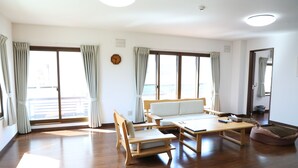 A spacious living room with a wooden floor, a sofa, a coffee table, and a bean bag. - Kashiwa House Furano (Furano)