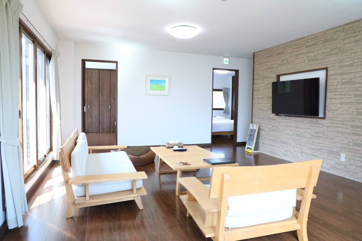 A modern room with wooden furniture, a flat-screen TV, and large windows.