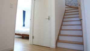 A bedroom with a bed, a white door, and a wooden staircase. - Kashiwa House Furano (Furano)