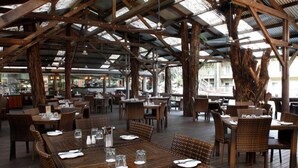 An outdoor restaurant with wooden tables and chairs, a high ceiling with metal beams, and a view of the street. - C215 Ramada Resort Deluxe King - Free Wifi (Port Douglas)
