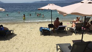 A beach with people swimming and sunbathing. There are umbrellas and lounge chairs on the sand. - Evia Dream (Istiaia-Aidipsos)