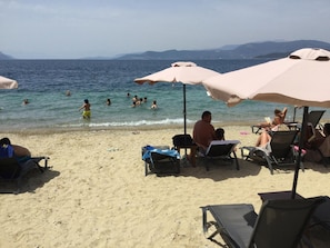 A beach with people swimming and sunbathing. There are umbrellas and lounge chairs on the sand. - Evia Dream (Istiaia-Aidipsos)