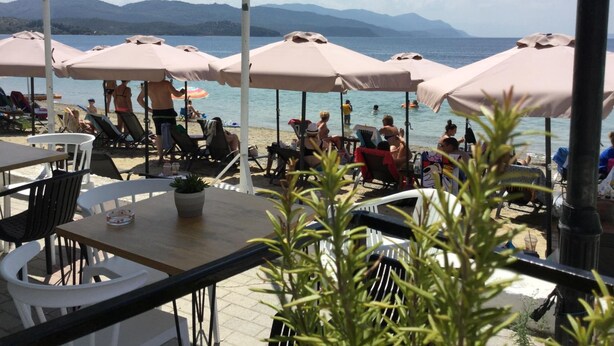 A beachside café with outdoor seating, umbrellas, and a view of the sea and mountains. - Evia Dream (Istiaia-Aidipsos)