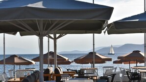A seaside restaurant with outdoor seating, umbrellas, and a view of the sea and distant mountains. - Evia Dream (Istiaia-Aidipsos)