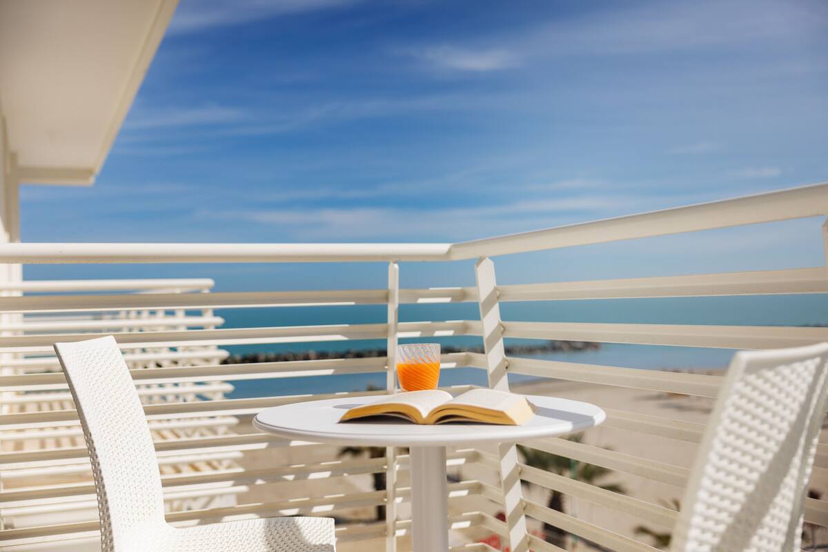 A white outdoor seating area with a table, a chair, and an open book.