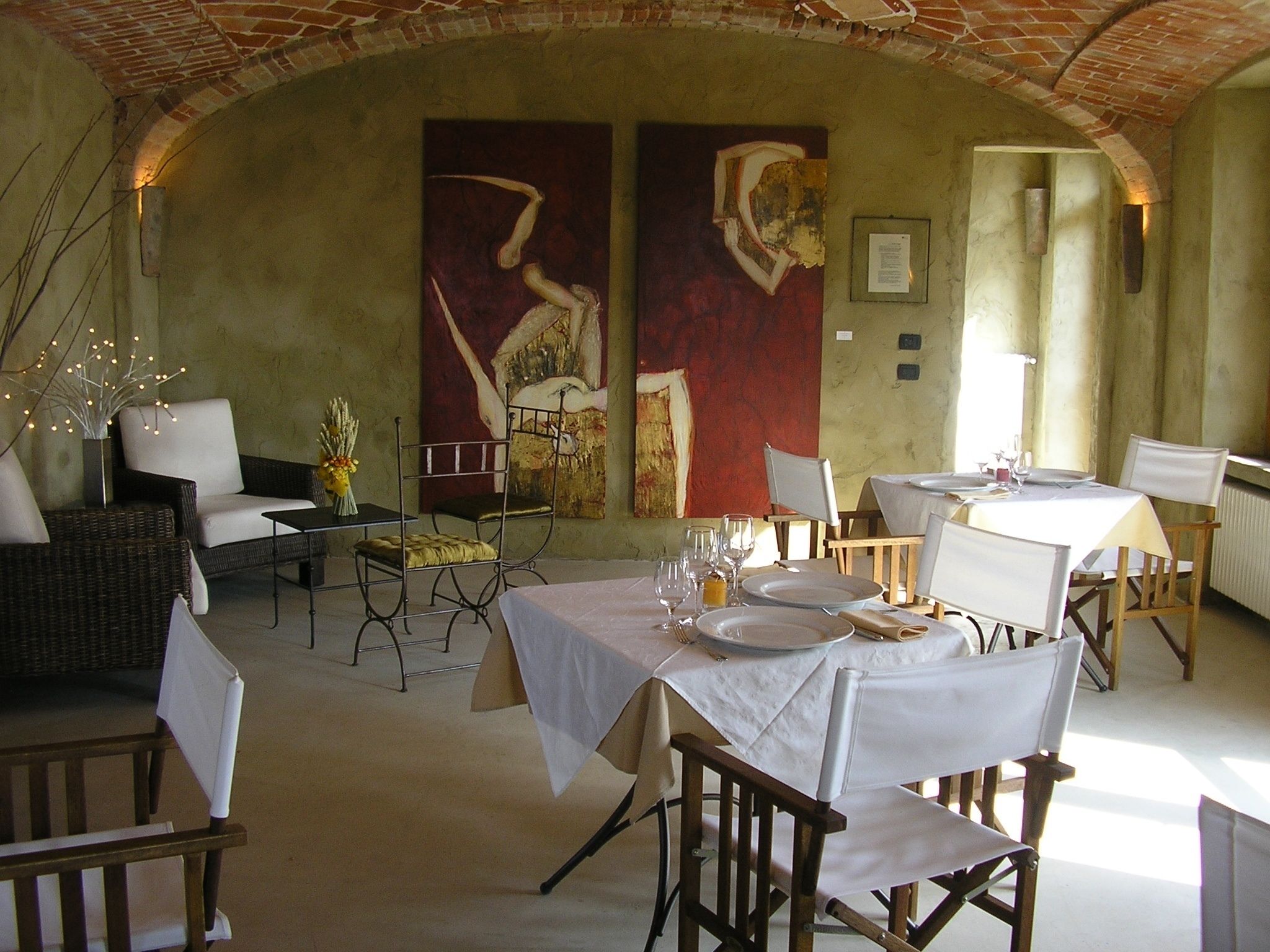 A restaurant with a rustic brick ceiling, white tablecloths, and a mix of wicker and wooden chairs.