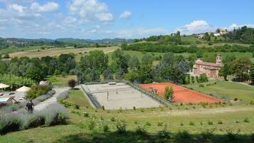 A tennis court surrounded by lush greenery and a church with a bell tower.