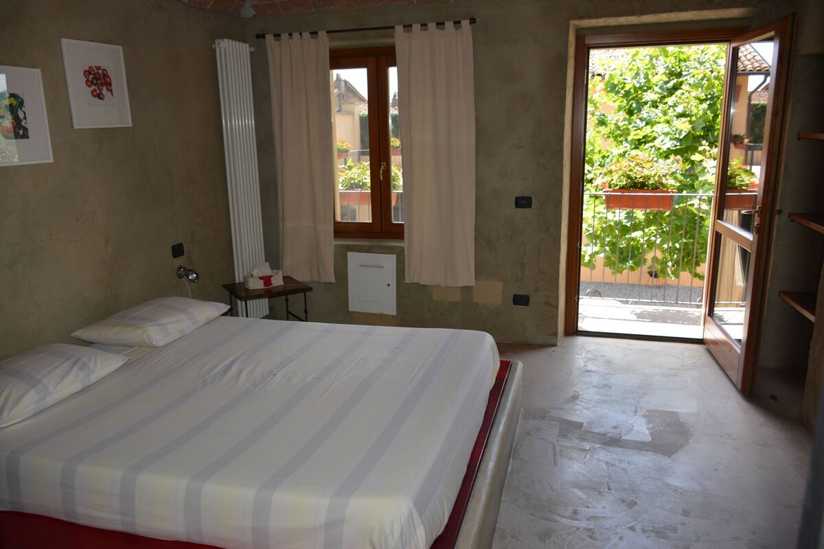 A bedroom with a bed, a nightstand, a window with curtains, and a view of the outside.