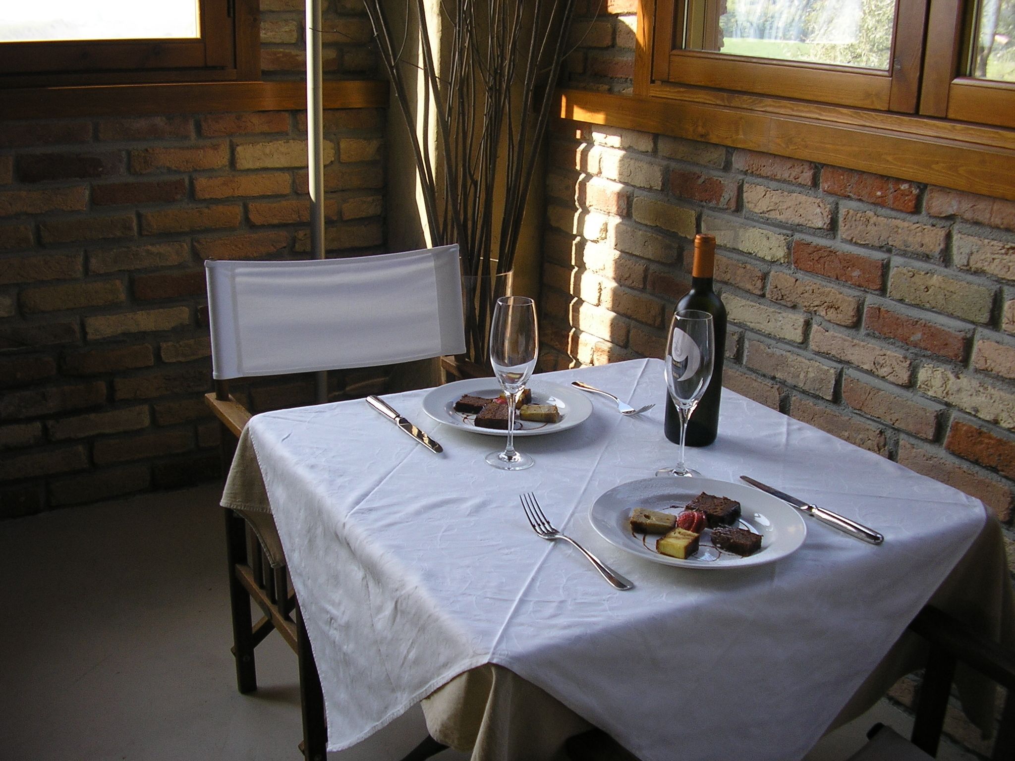 Mesa lista para dos personas, con platos de comida, copas de vino y cubiertos.