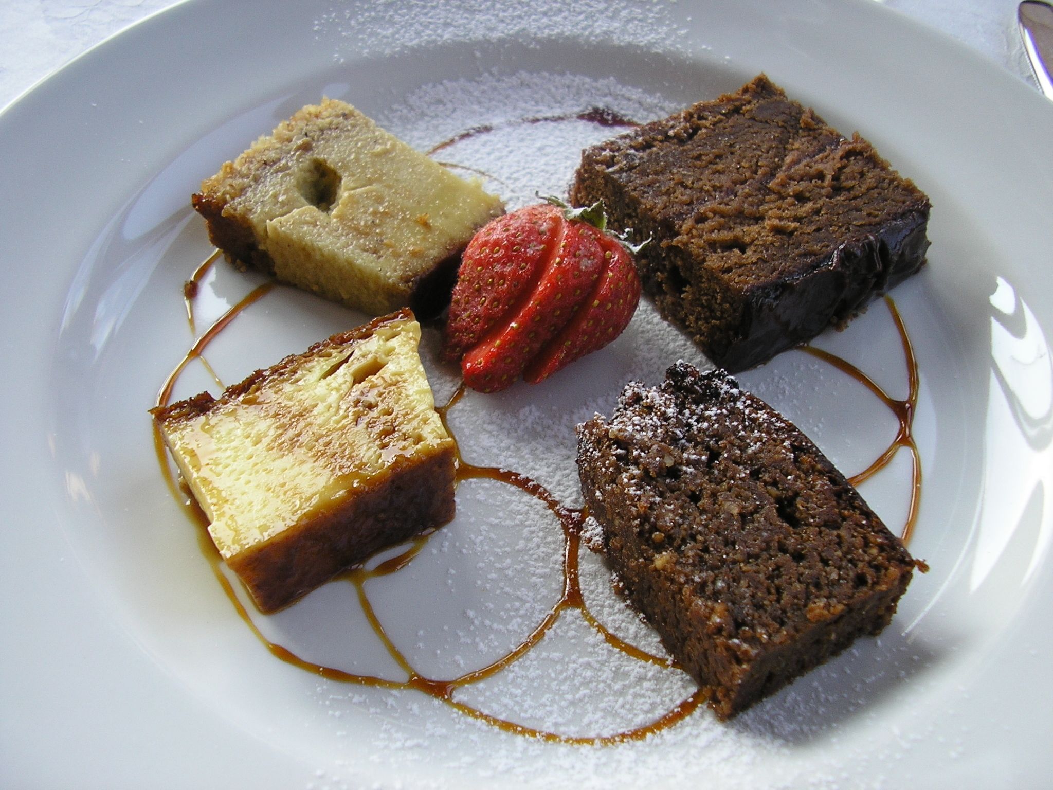Un plato de postres con varios tipos de pastel y una fresa.