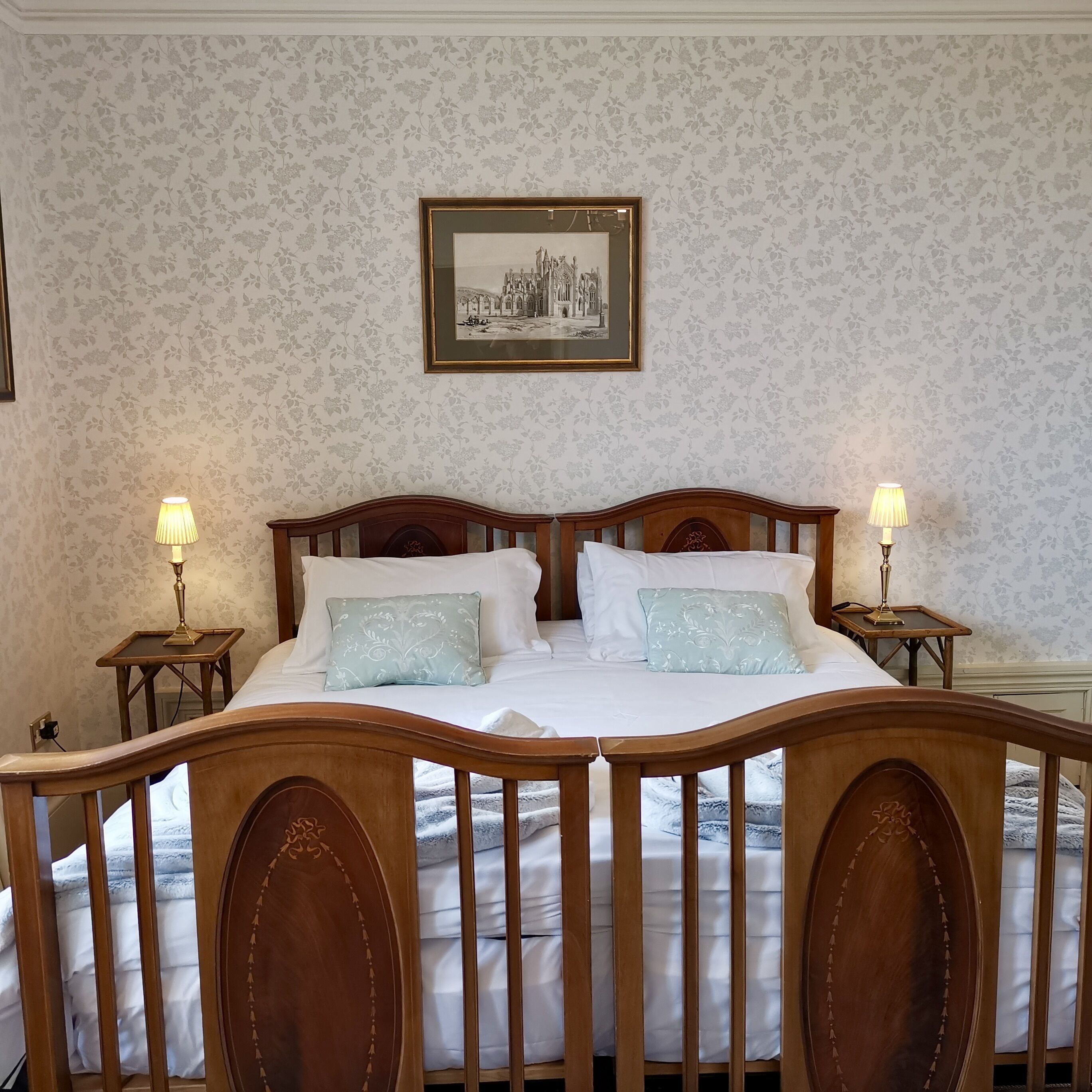 A neatly made bed with two pillows, a wooden headboard, and two bedside lamps.