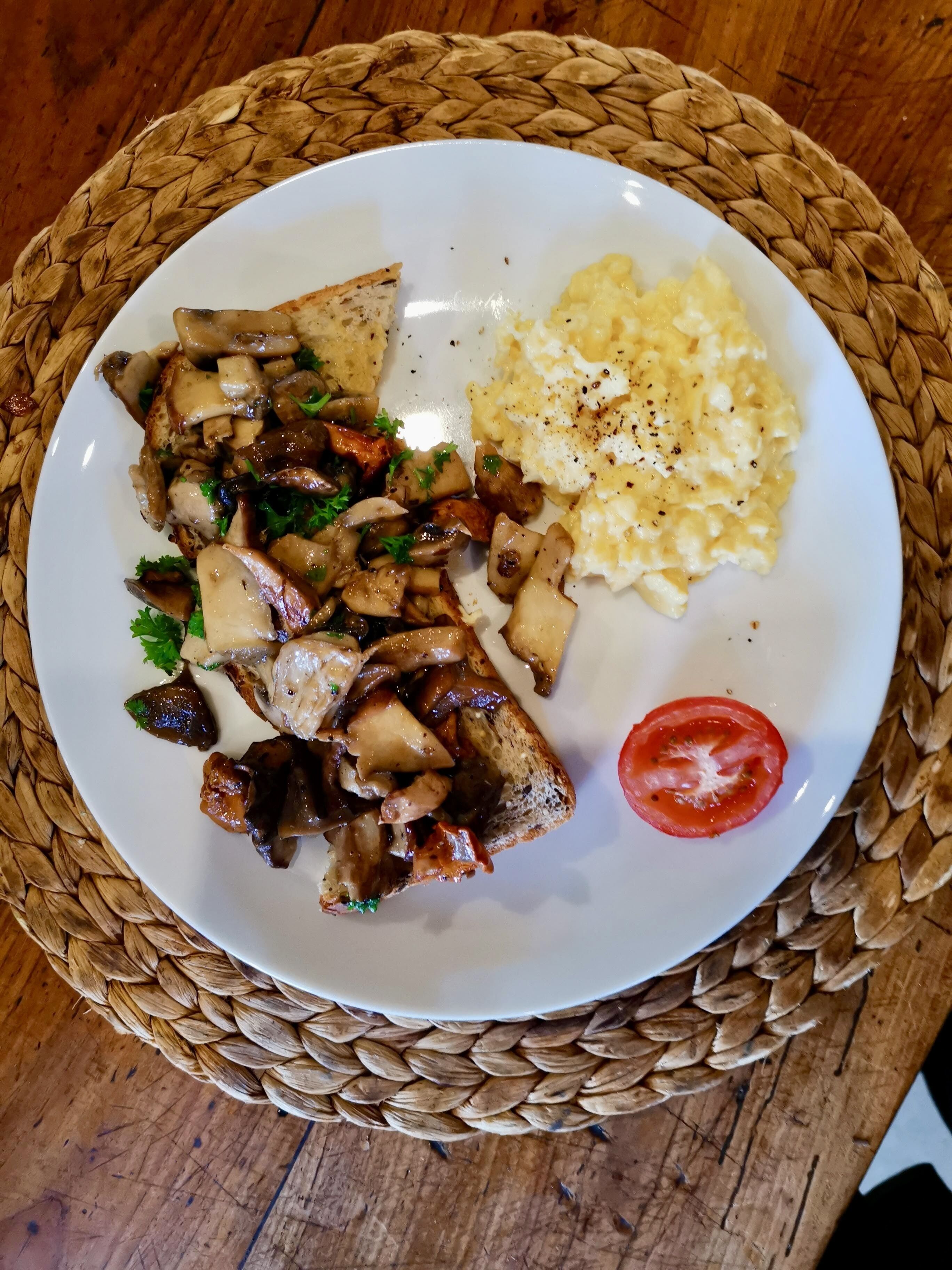 Een bord met gegrilde champignons, roerei en een plak tomaat op een geweven onderzetter.