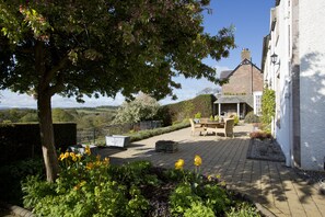 A garden with a tree, flowers, and a patio area with a table and chairs. - Bowden House B&B (Melrose)