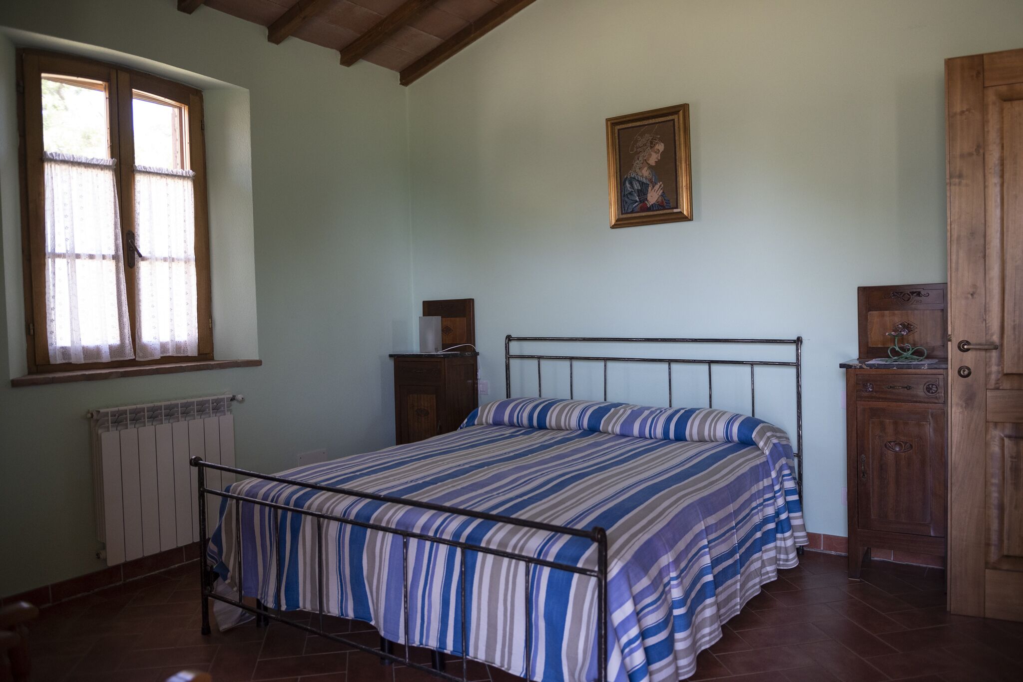 A bedroom with a metal bed frame, a radiator, a wooden cabinet, and a window with curtains.
