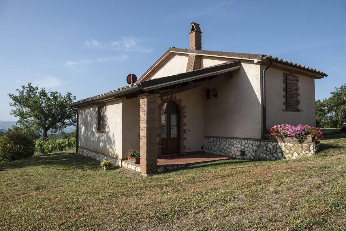Uma casa térrea com alicerce de pedra, telhado telhado e pequena varanda com coluna de tijolo.