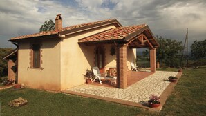 Una casa de un piso con techo de tejas, un porche cubierto con mobiliario exterior, y un sendero de piedra que conduce a la entrada.