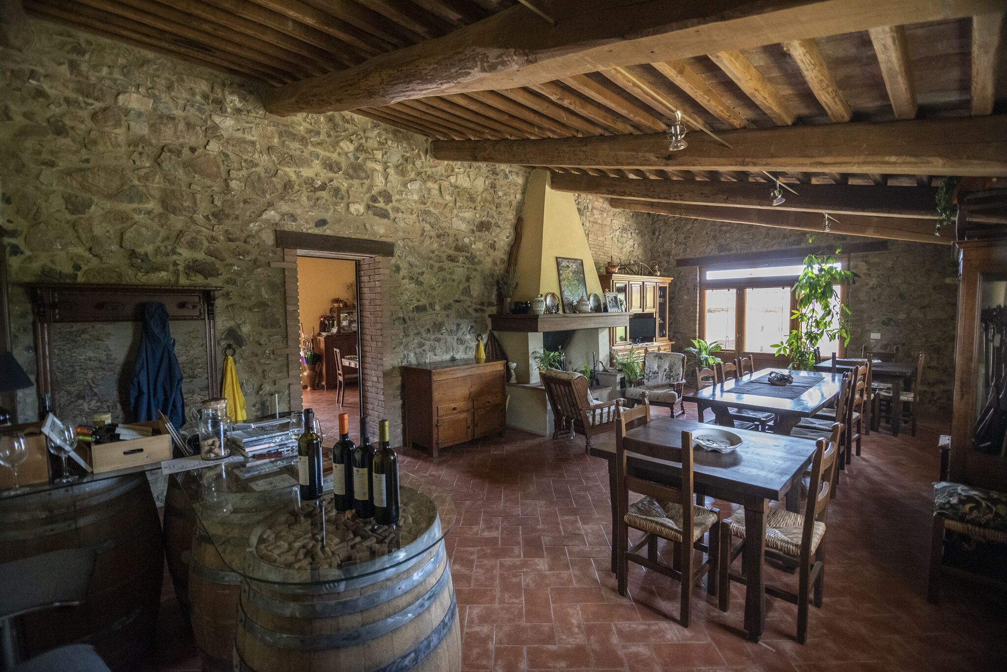 Un intérieur rustique avec des murs en pierre, des poutres en bois, un coin repas avec une table et des chaises, et un bar avec des bouteilles et des verres.