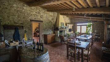 Un intérieur rustique avec des murs en pierre, des poutres en bois, un coin repas avec une table et des chaises, et un bar avec des bouteilles et des verres.