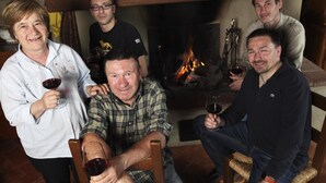 Un grupo de personas sentadas alrededor de una chimenea en una habitación con muebles de madera y piso de baldosas.