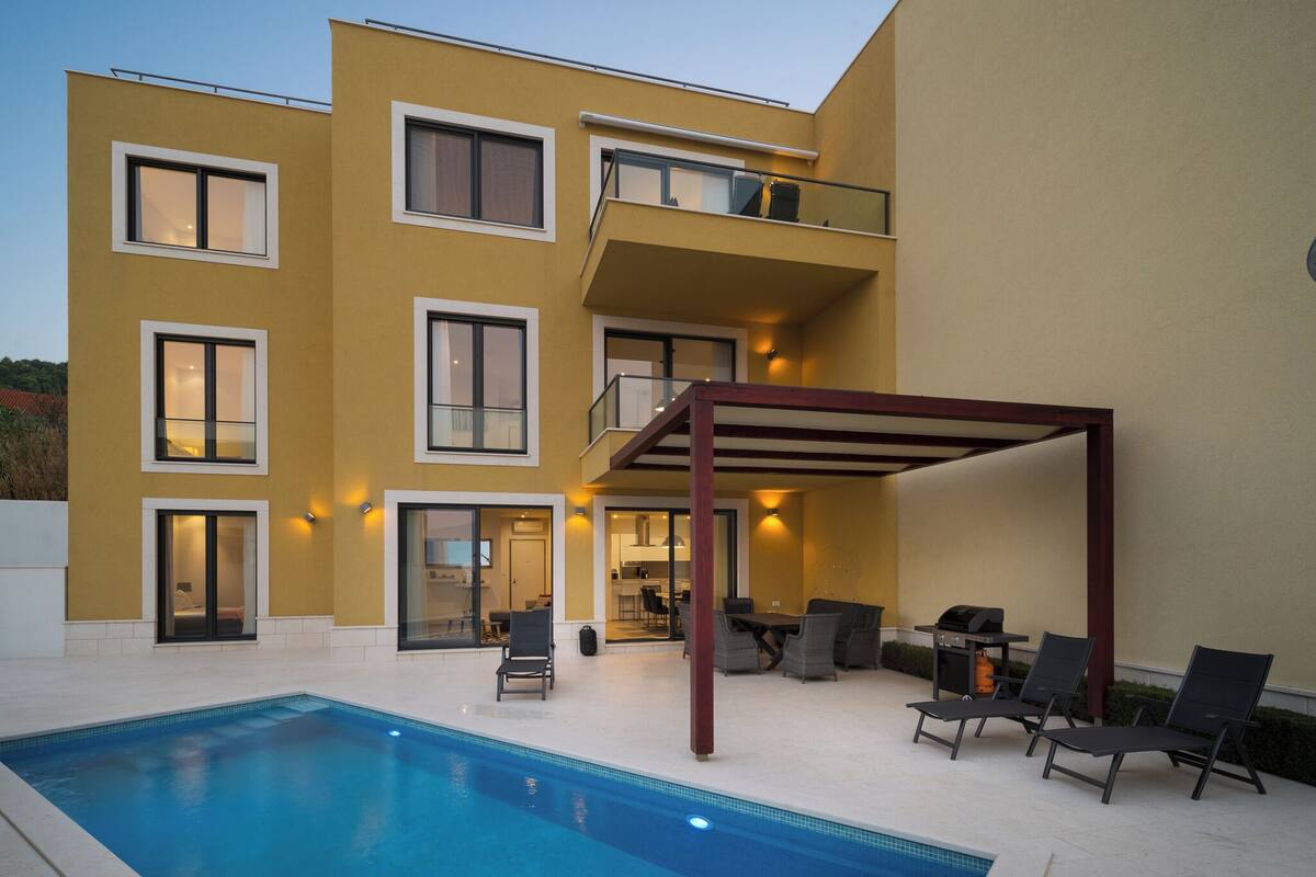 A modern two-story building with a swimming pool, outdoor seating, and a covered patio area.