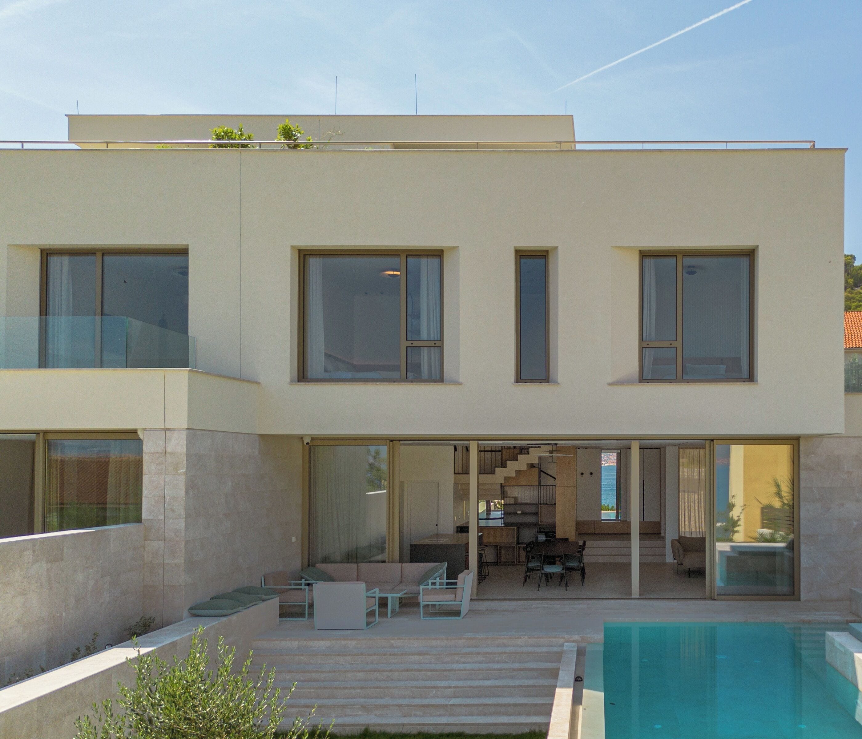 A modern two-story house with a swimming pool, outdoor seating, and a staircase leading to the upper floor.