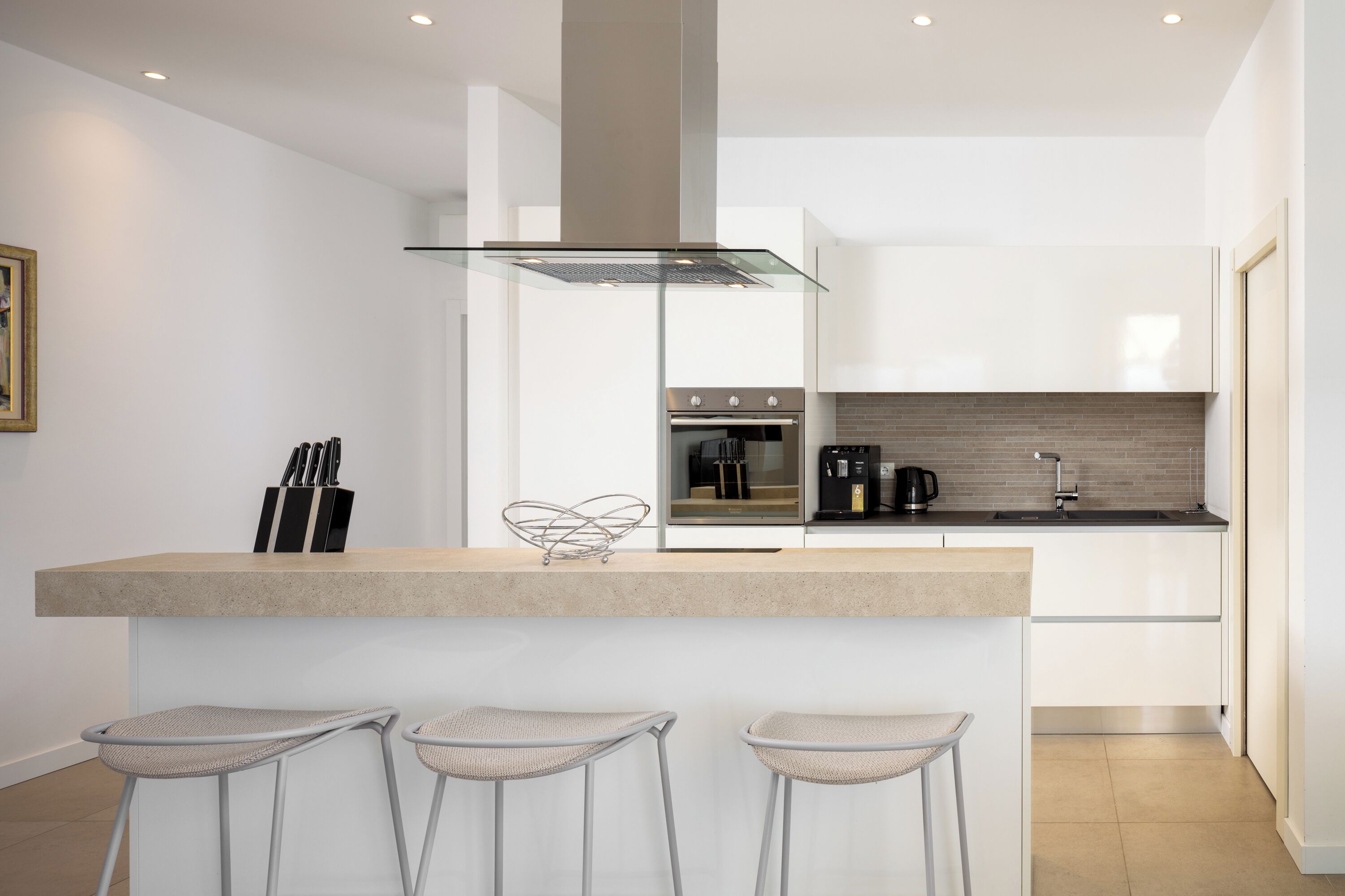 Una cucina moderna con isola centrale, sgabelli da bar, elettrodomestici in acciaio inossidabile e cappa in vetro.