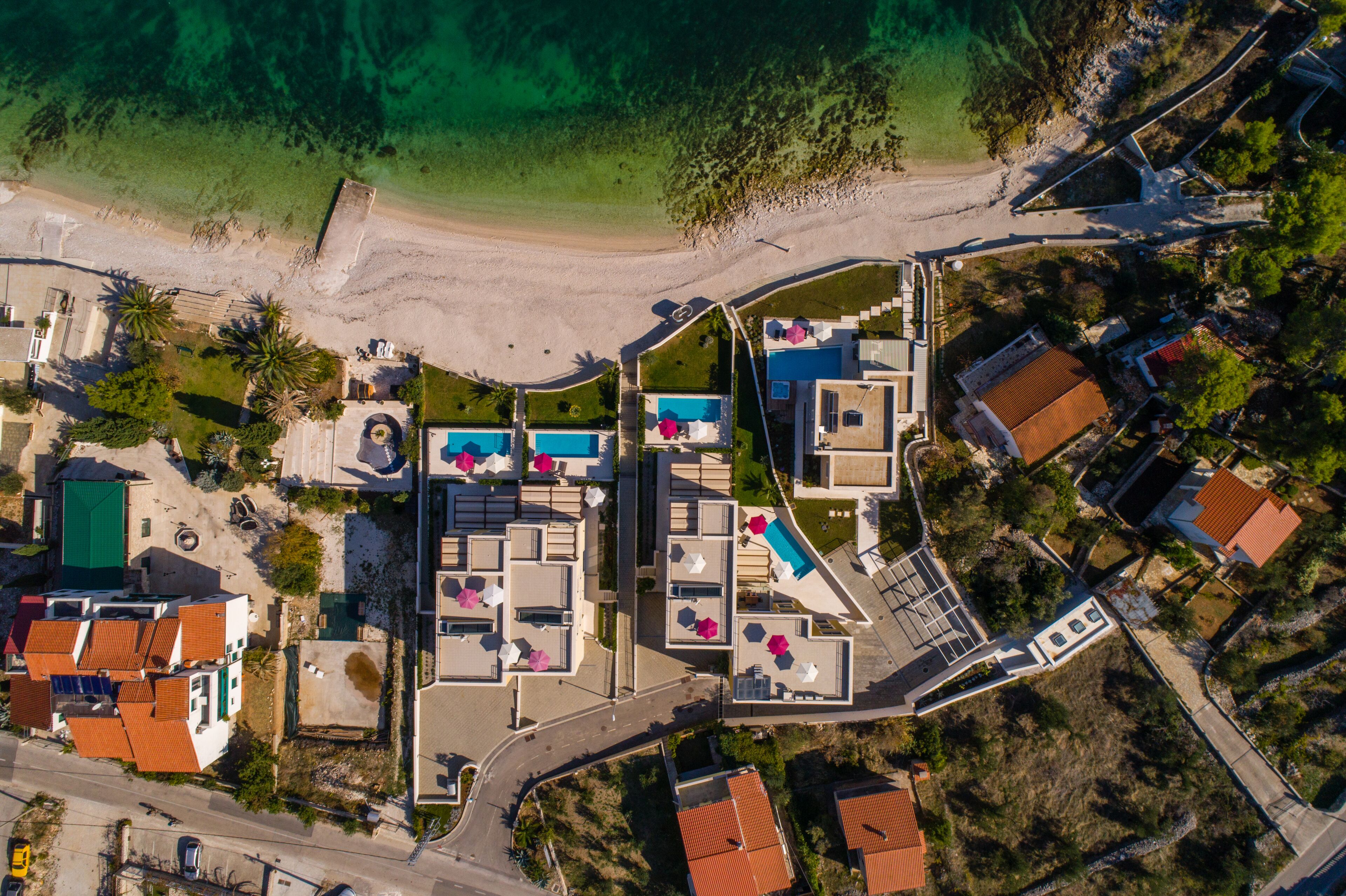 An aerial view of a coastal resort with a swimming pool, beach access, and a variety of buildings.