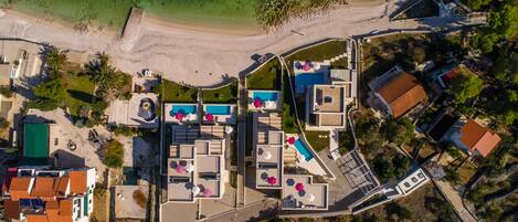 An aerial view of a coastal resort with a swimming pool, beach access, and a variety of buildings.