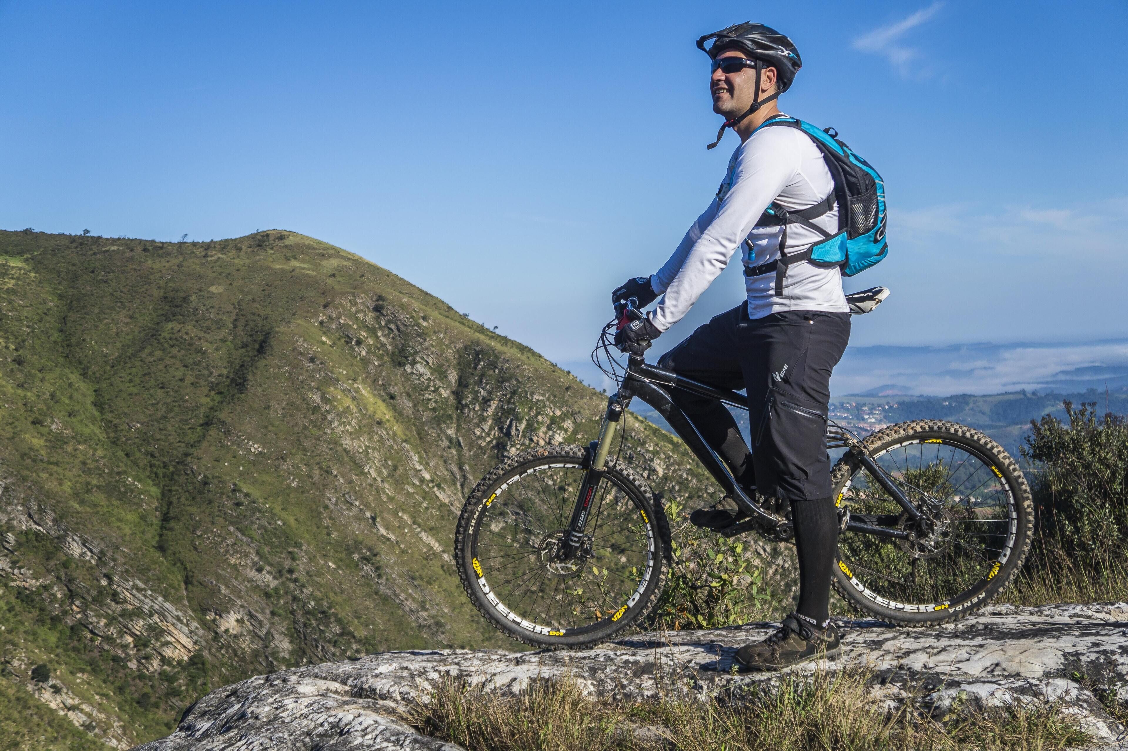 Un ciclista de montaña en un saliente rocoso con vistas despejadas a un paisaje montañoso.