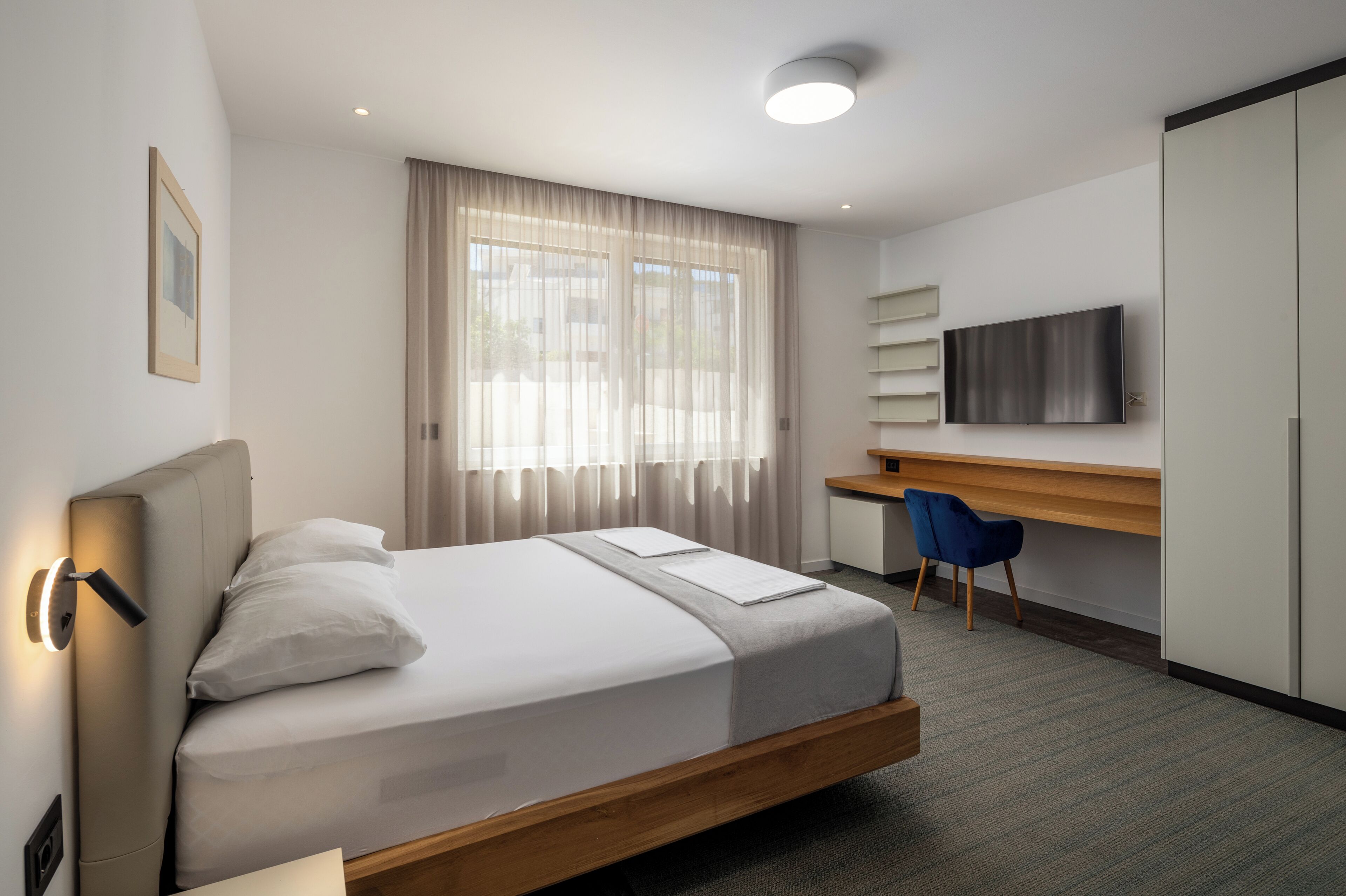 Ein modernes Hotelzimmer mit Bett, Schreibtisch, Stuhl, Fernseher und Kleiderschrank.