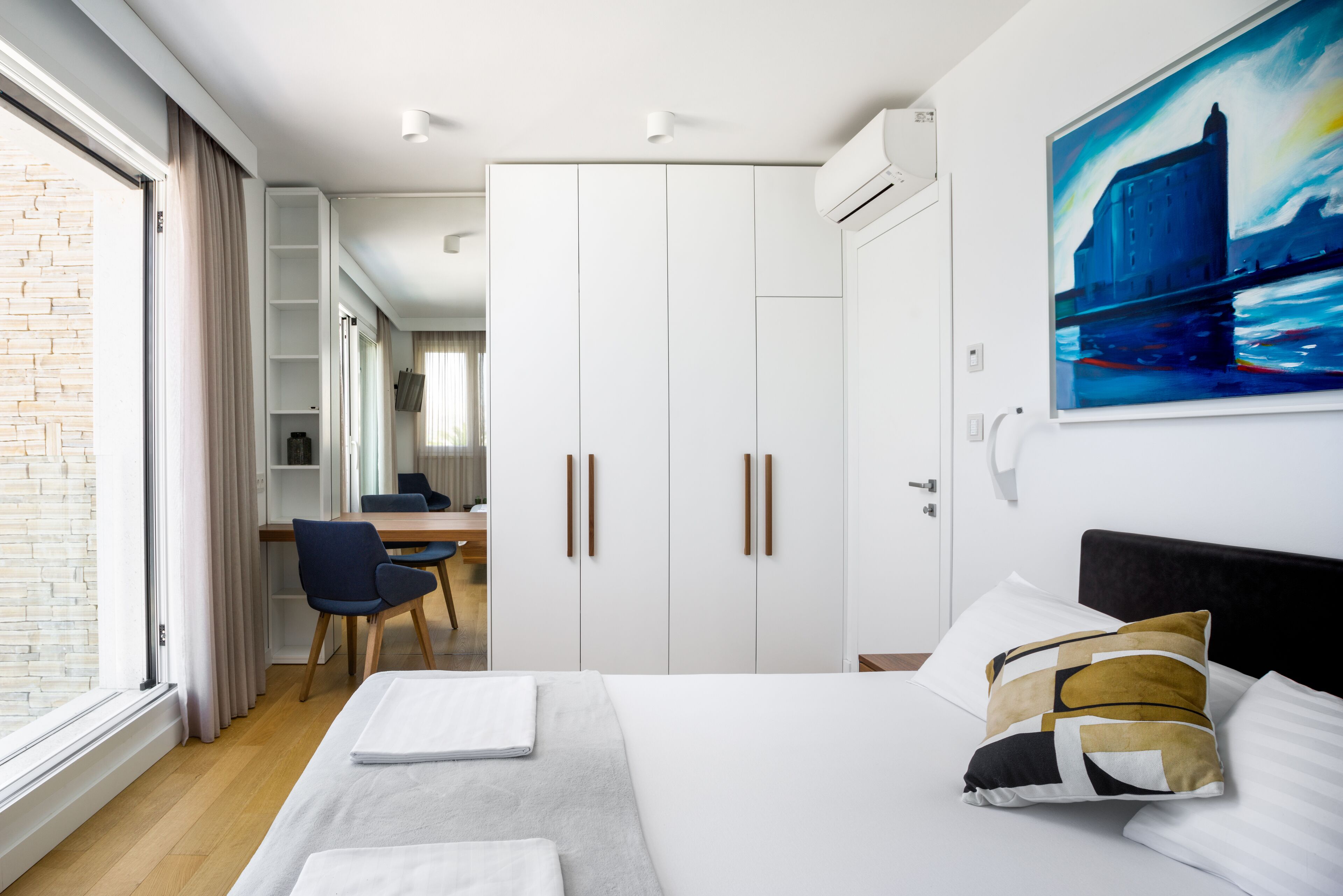 Moderni hotellihuone, jossa on sänky, työpöytä ja vaatekaappi.