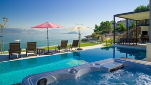 Un área de piscina con sillones de descanso y sombrillas, un jacuzzi y vistas al mar.