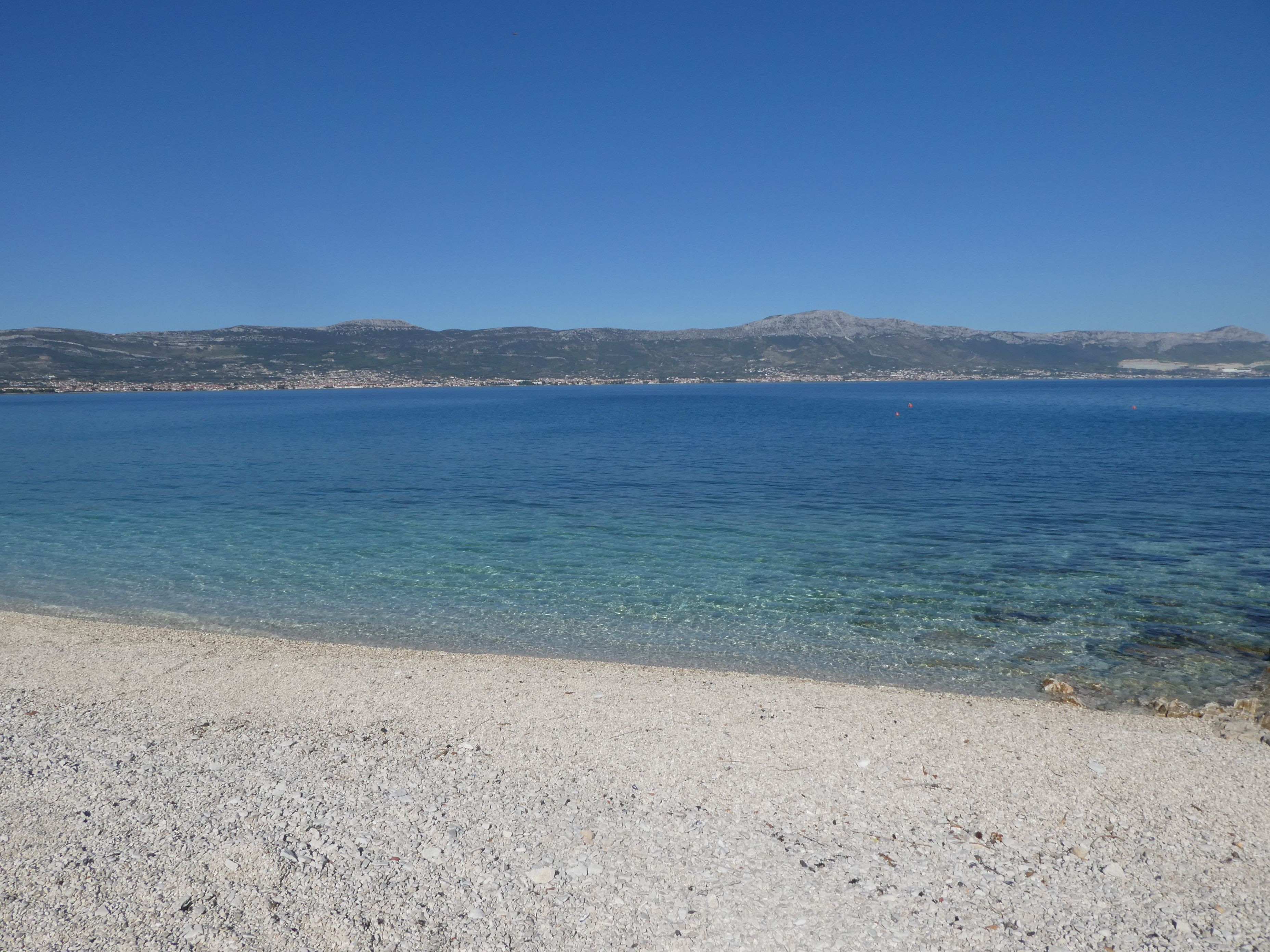 Ein freier Blick auf einen Kiesstrand, der zu einem ruhigen Meer mit fernen Bergen führt.