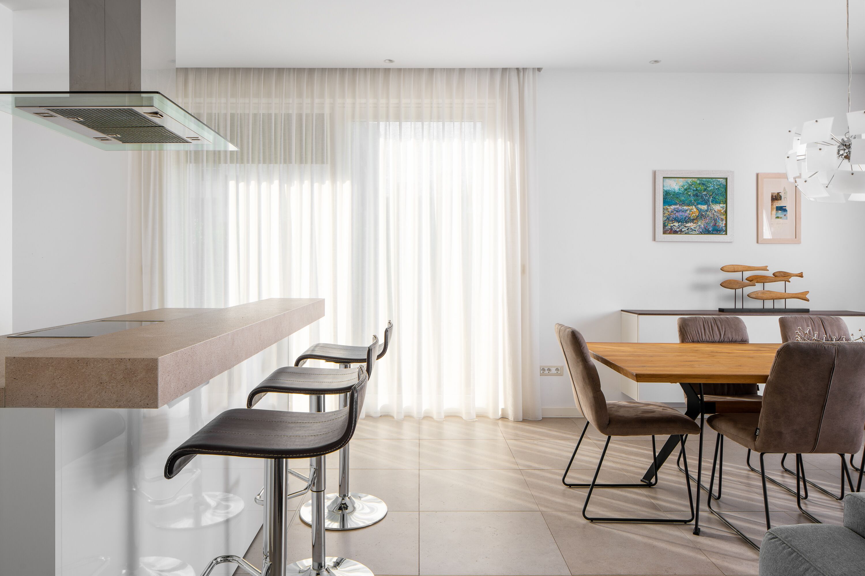 A modern kitchen with a bar area, a dining table with chairs, and artwork on the wall.