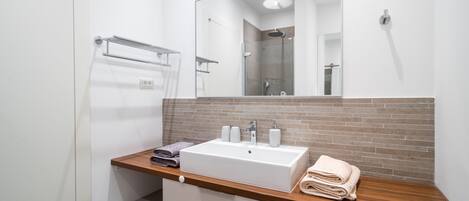 Ein modernes Badezimmer mit Waschbecken, Holztischplatte und großem Spiegel.