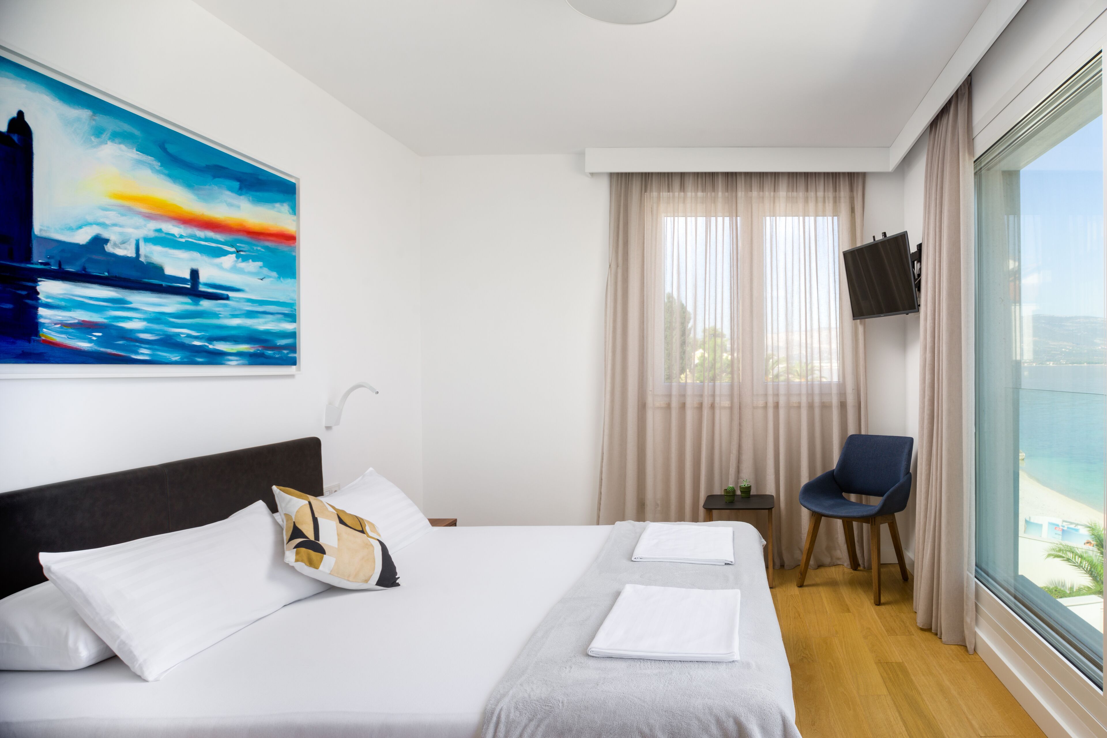 A hotel room with a large bed, a chair, a TV, and a painting on the wall.