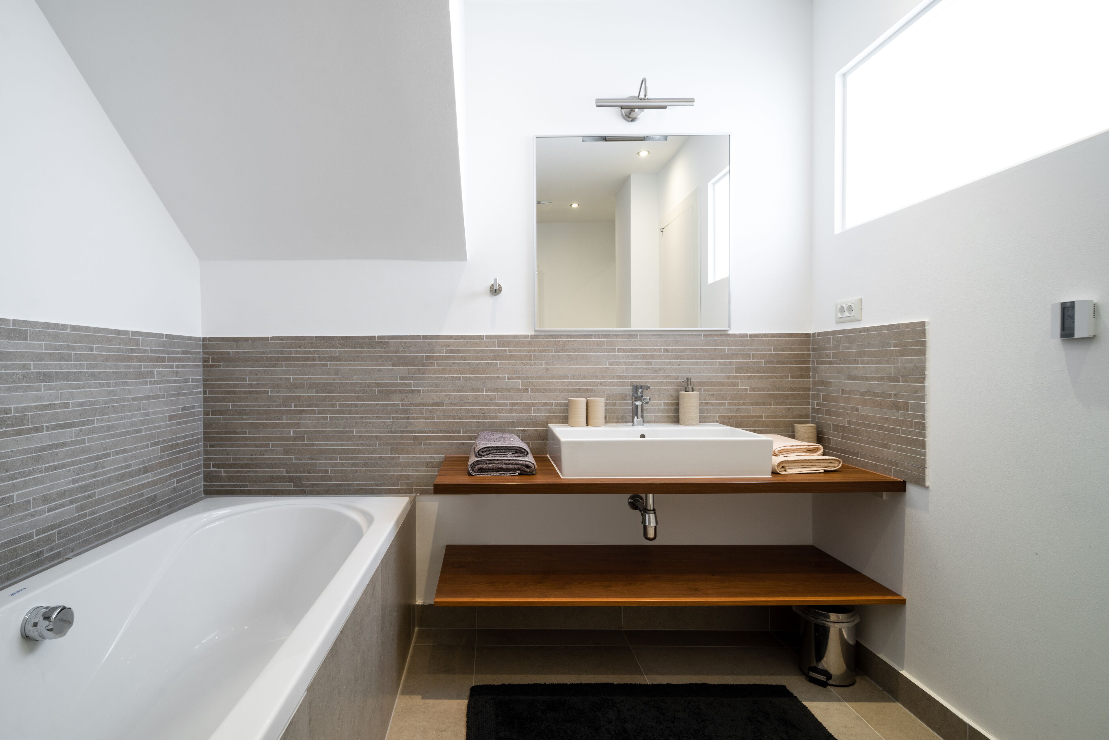 Ein modernes Badezimmer mit einer freistehenden Badewanne, einem Holzbadezimmer-Waschtisch und einem großen Spiegel darüber.