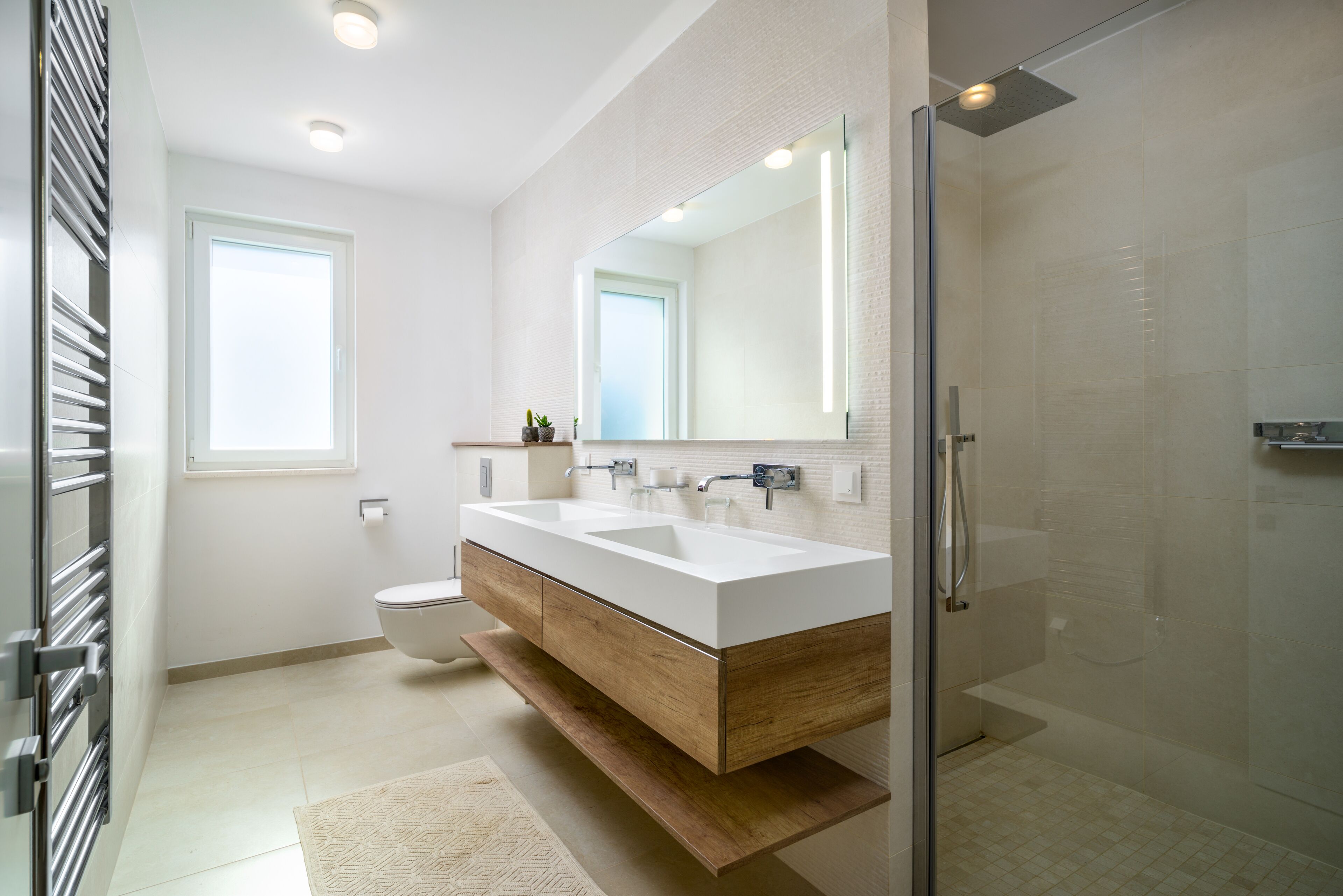 A modern bathroom with a double sink vanity, a glass shower enclosure, and a toilet.