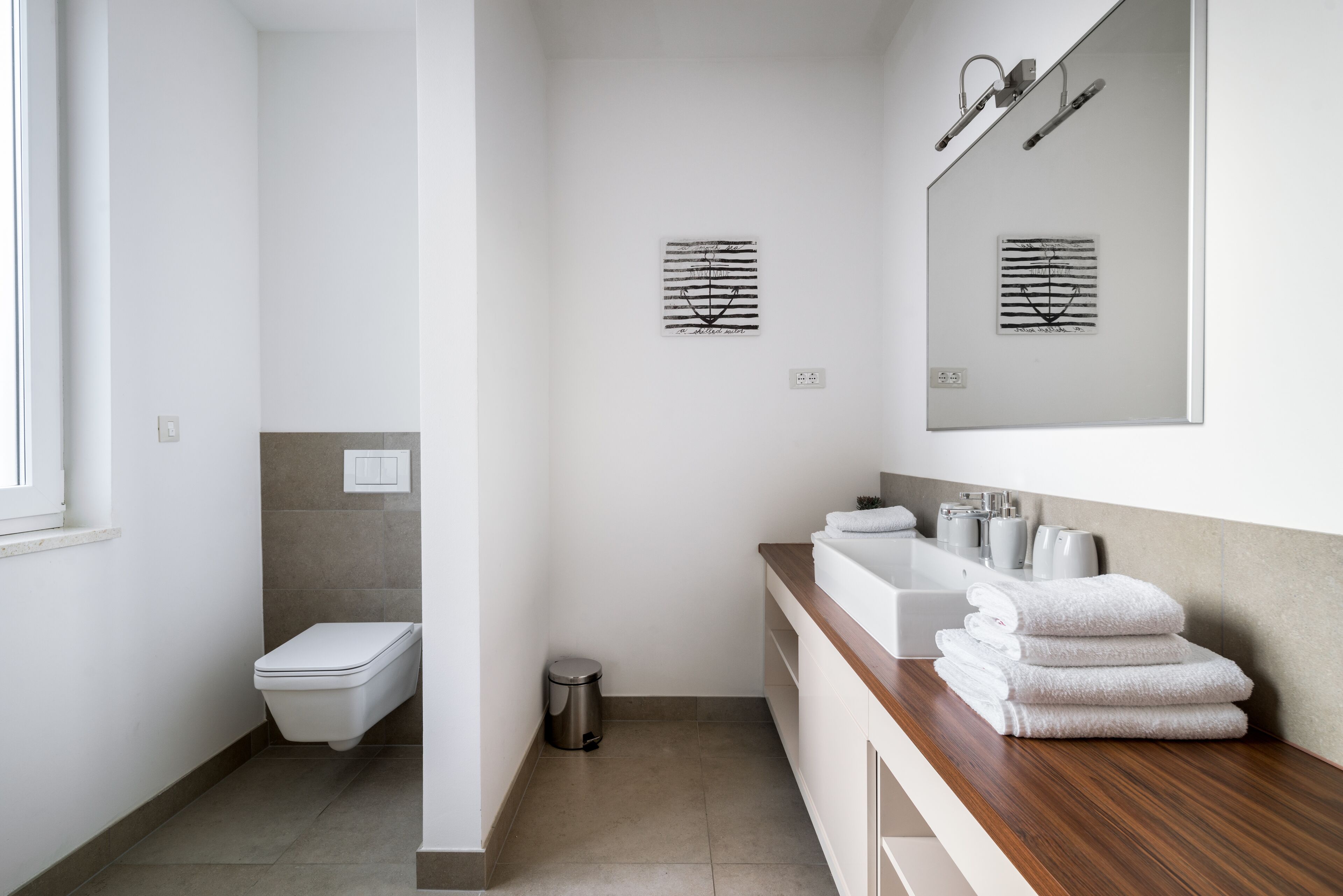 A modern bathroom with a toilet, sink, and mirror. There are towels stacked on the counter.