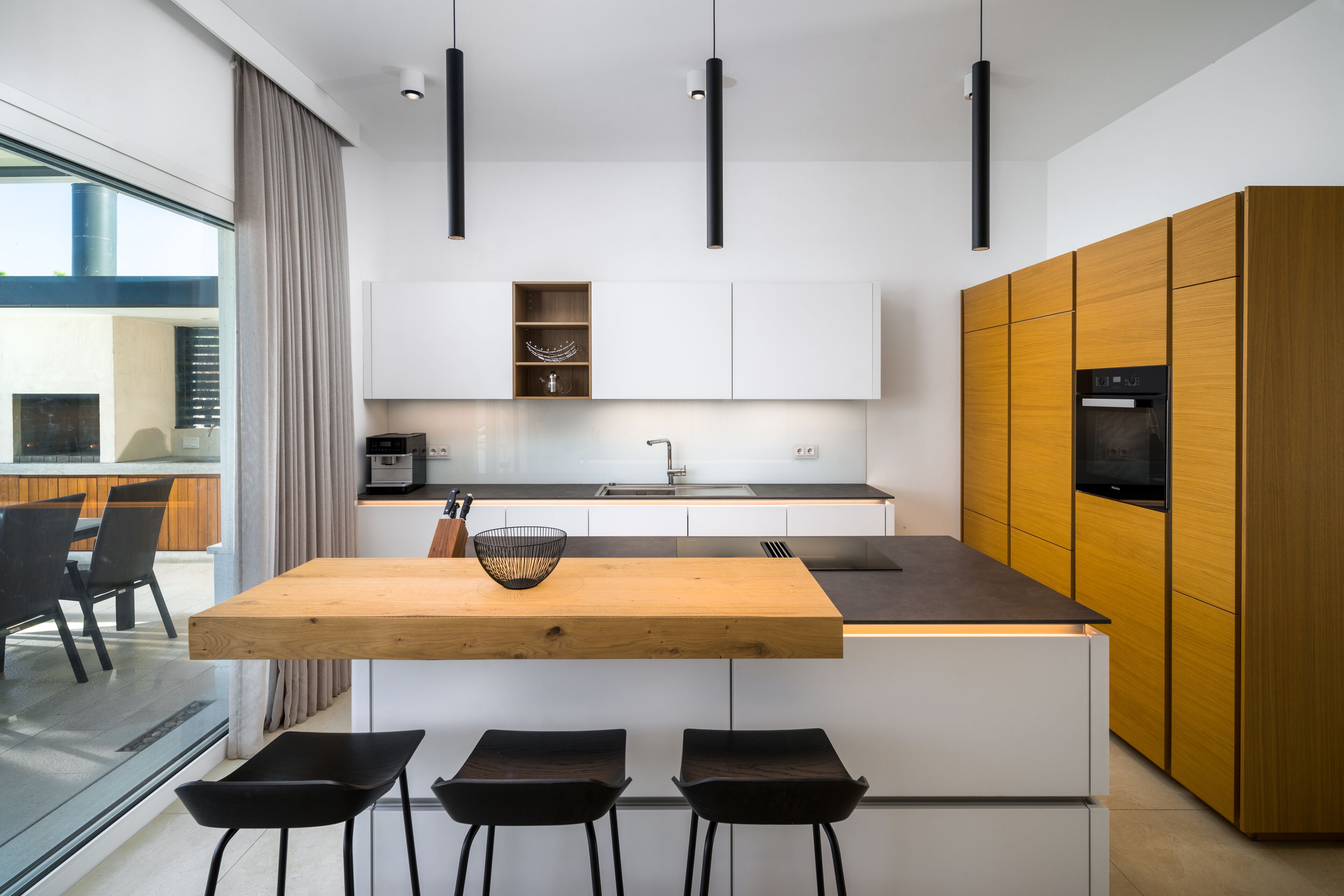 A modern kitchen with a wooden island, black bar stools, and built-in appliances.