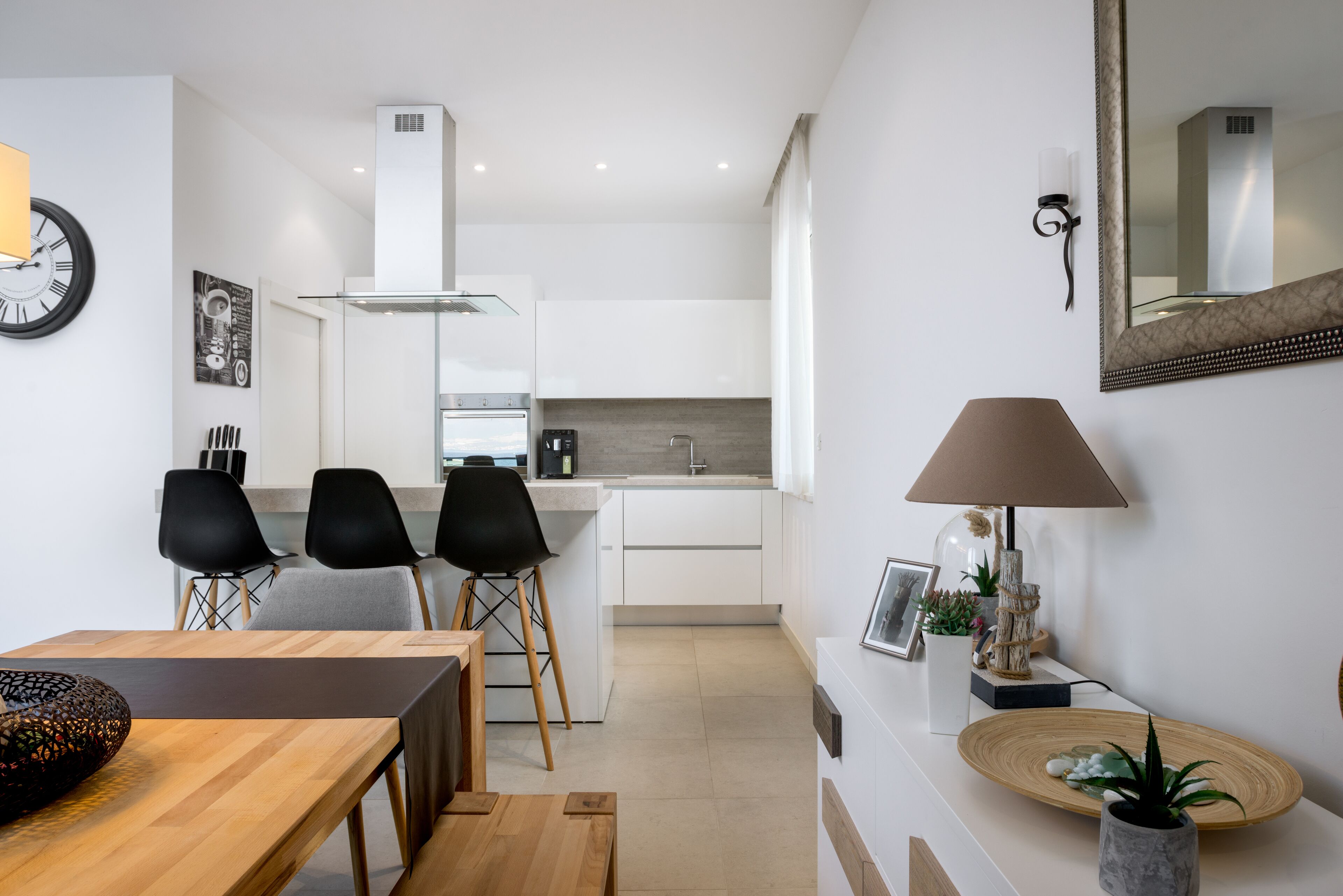 A modern kitchen with white cabinets, a built-in stove, and a dining area with a wooden table and chairs.