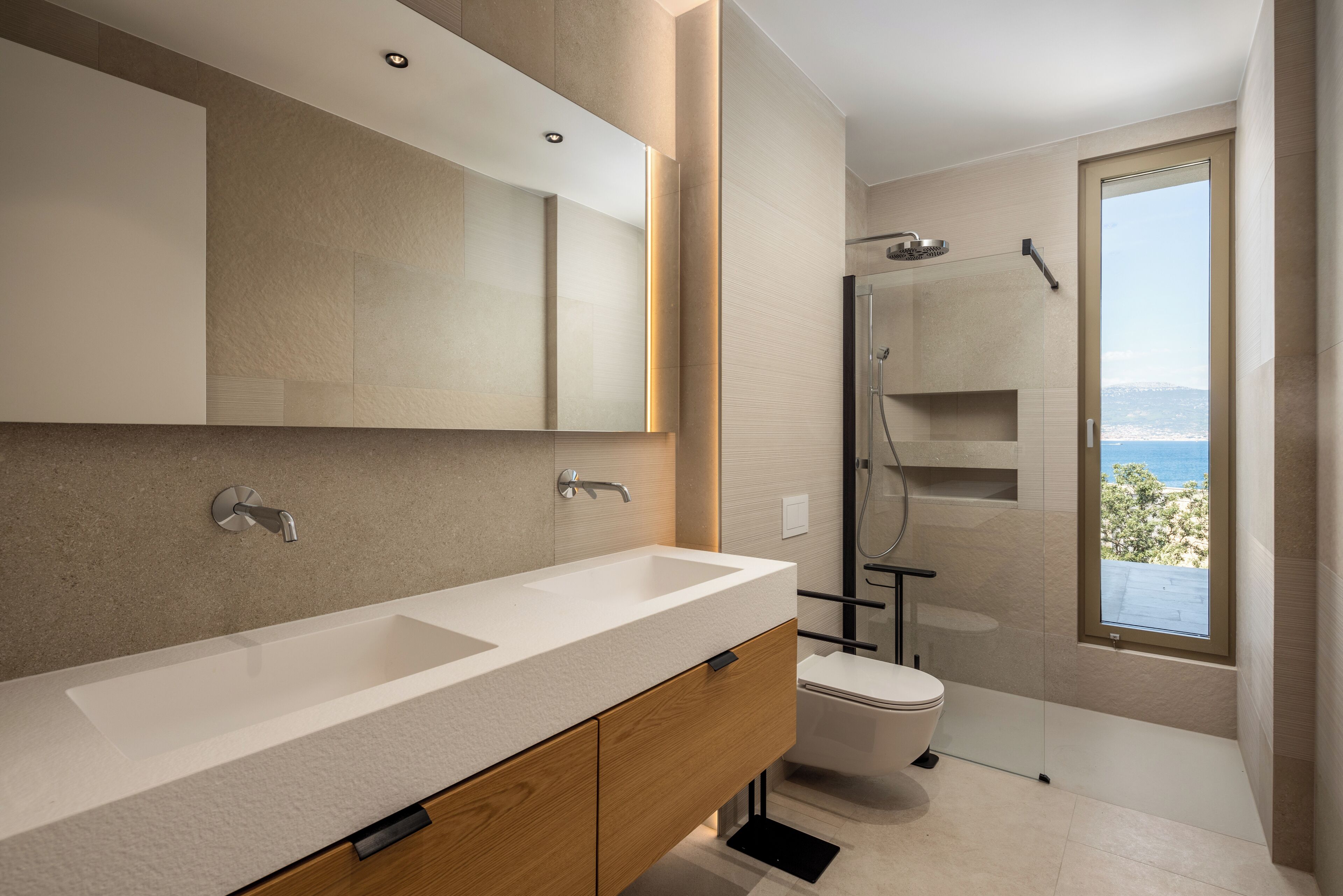 A modern bathroom with a large mirror, dual sinks, a toilet, and a shower.