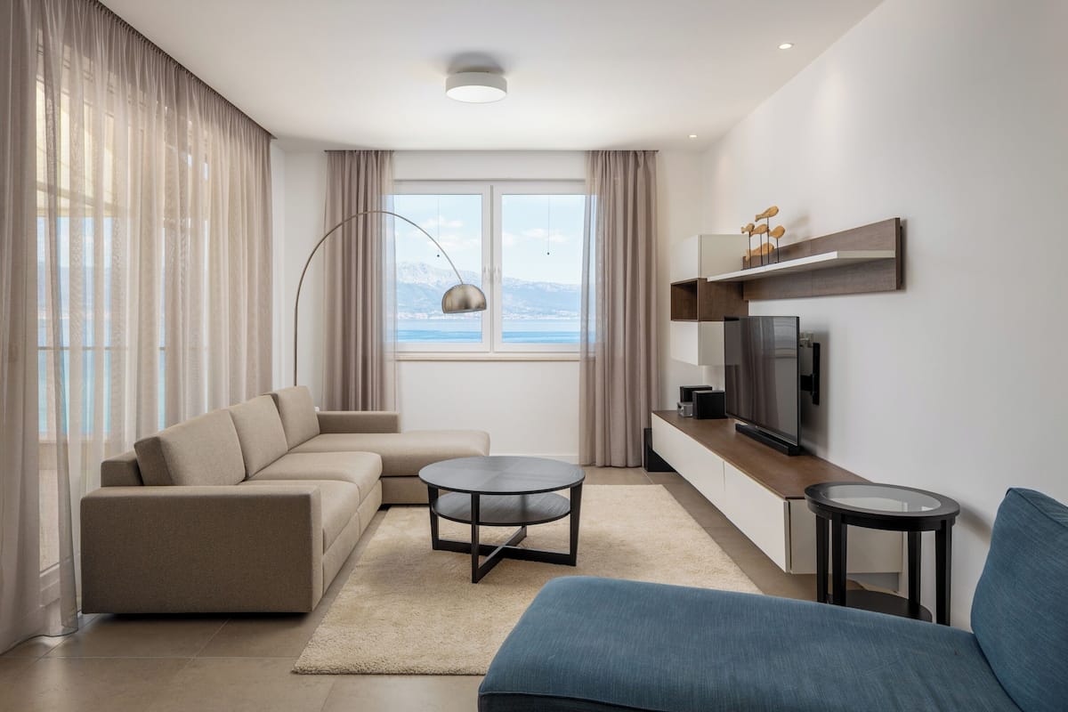 A modern living room with a sofa, a coffee table, a TV, and a view of the mountains.