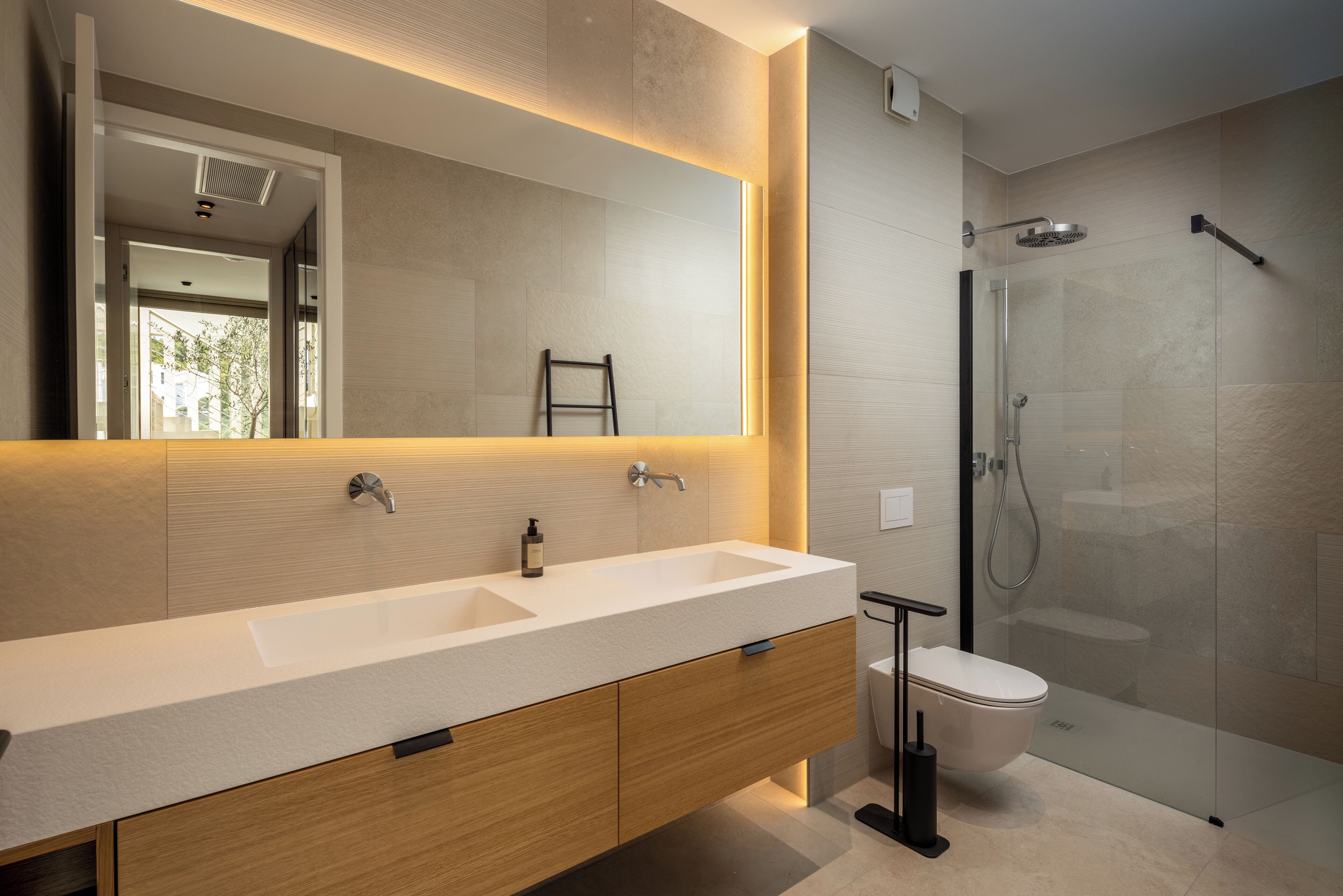 A modern bathroom with a large mirror, a double sink vanity, a toilet, and a glass-enclosed shower area.