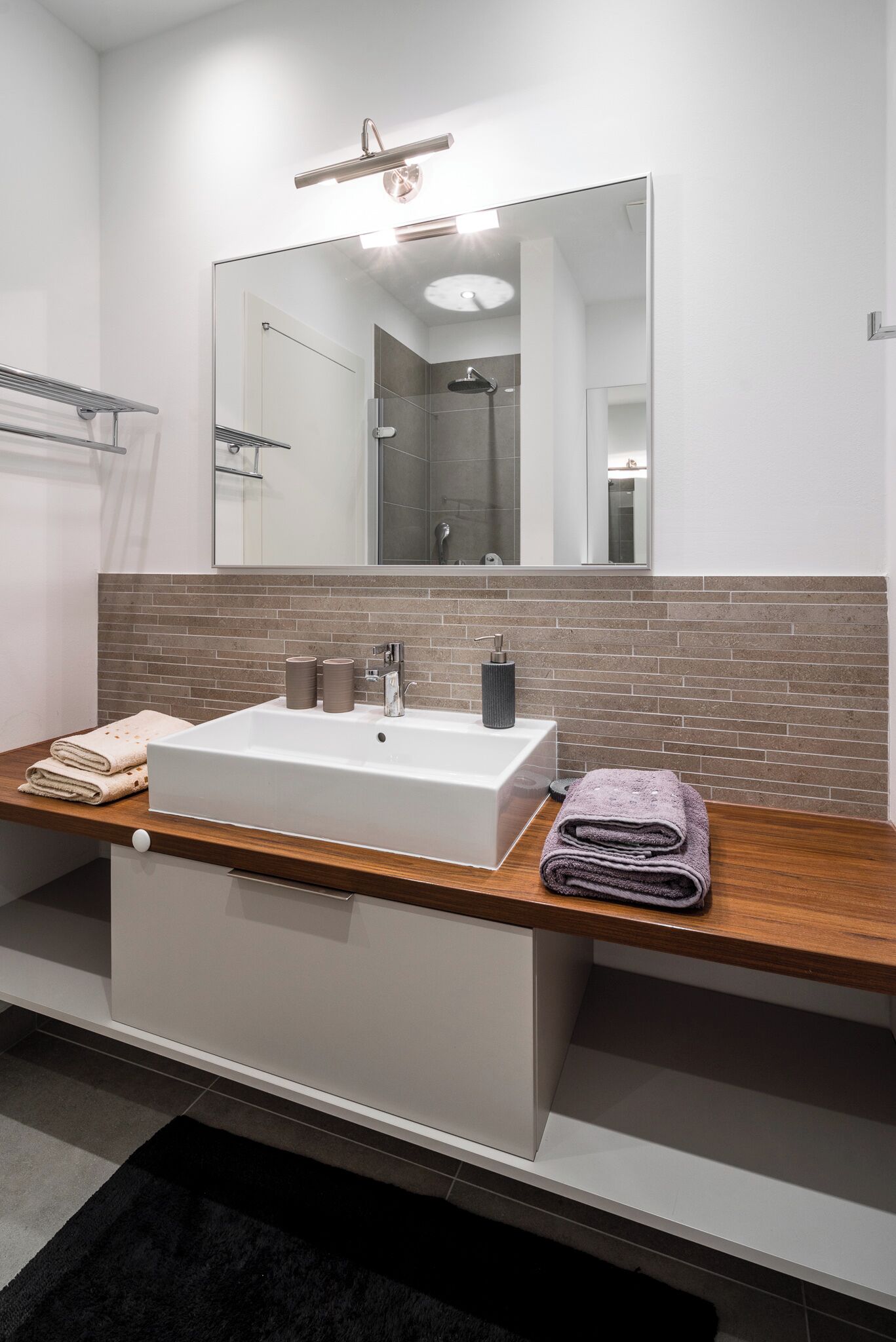 A modern bathroom with a large mirror, white sink, and wooden countertop.