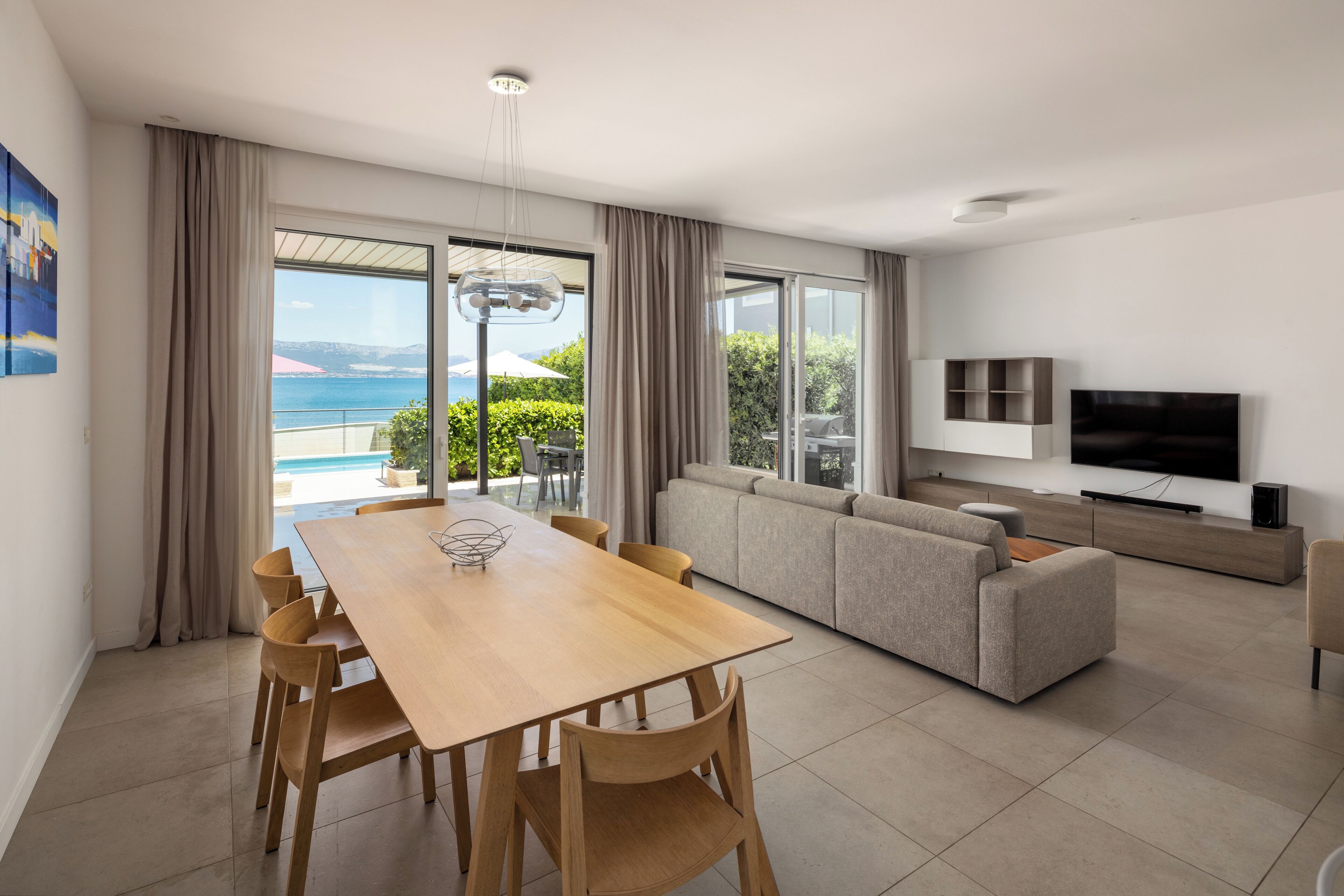 A modern living room with a wooden dining table, beige sofa, and a TV.